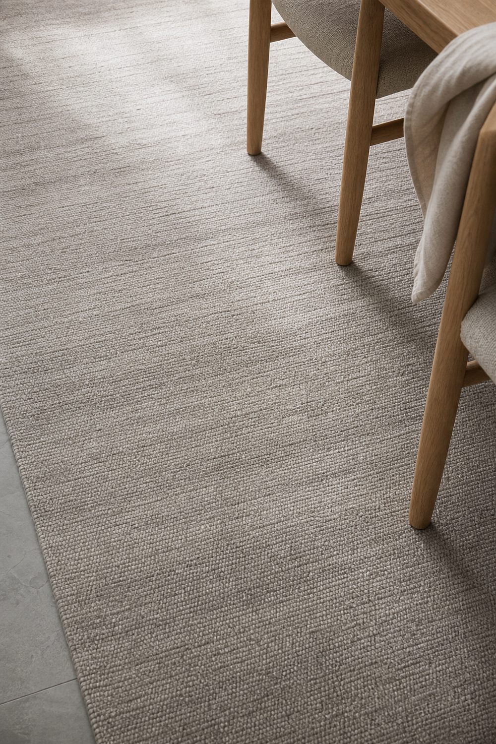 Low pile tonal greige Japandi rug with subtle weave variation beneath pale oak dining chairs and a linen throw