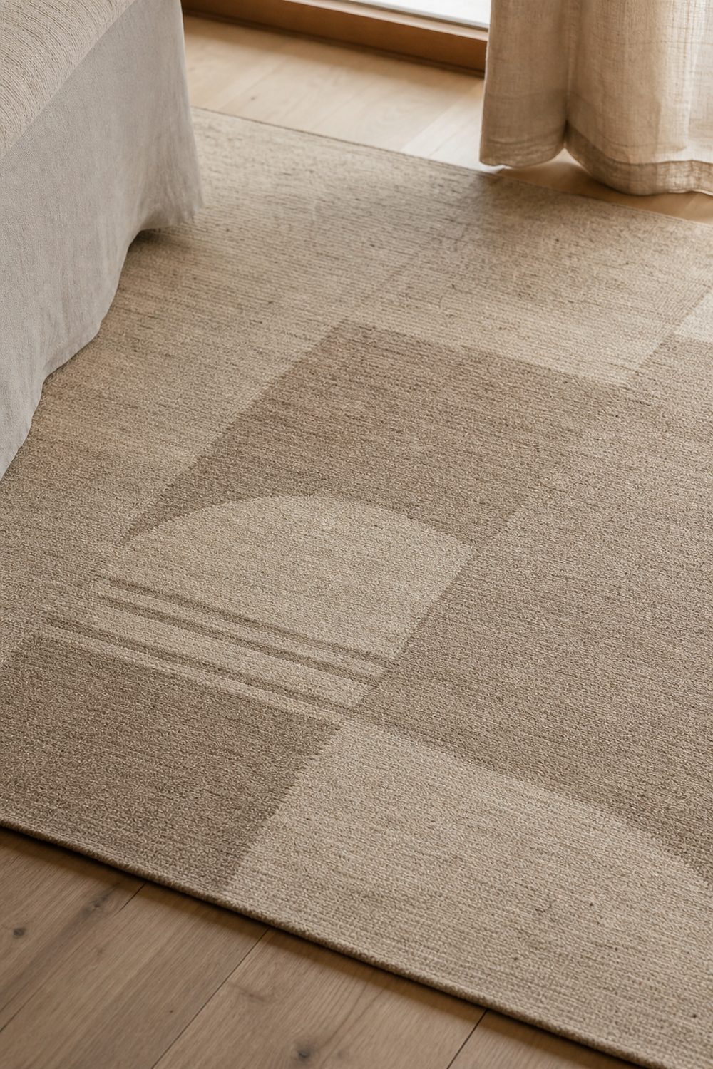 Muted geometric Japandi rug with low contrast arch and line shapes in oatmeal and taupe on a pale wood floor