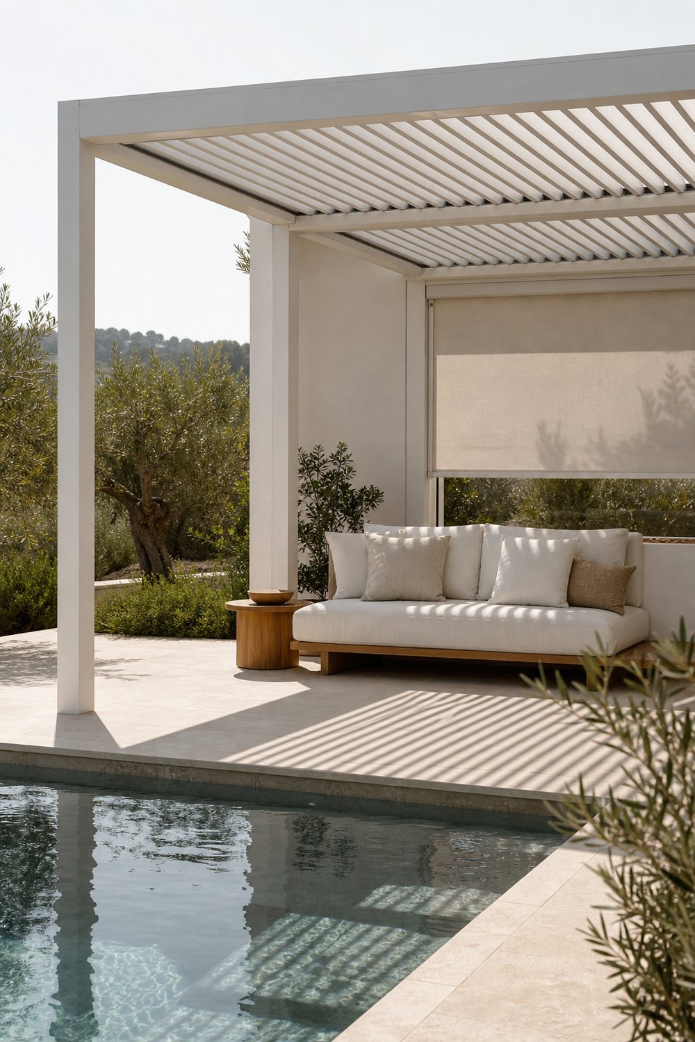 Open air small pool cabana built as a white aluminum pergola with slatted roof casting linear shadows, weatherproof cream sofa, teak side table, retractable shade panel