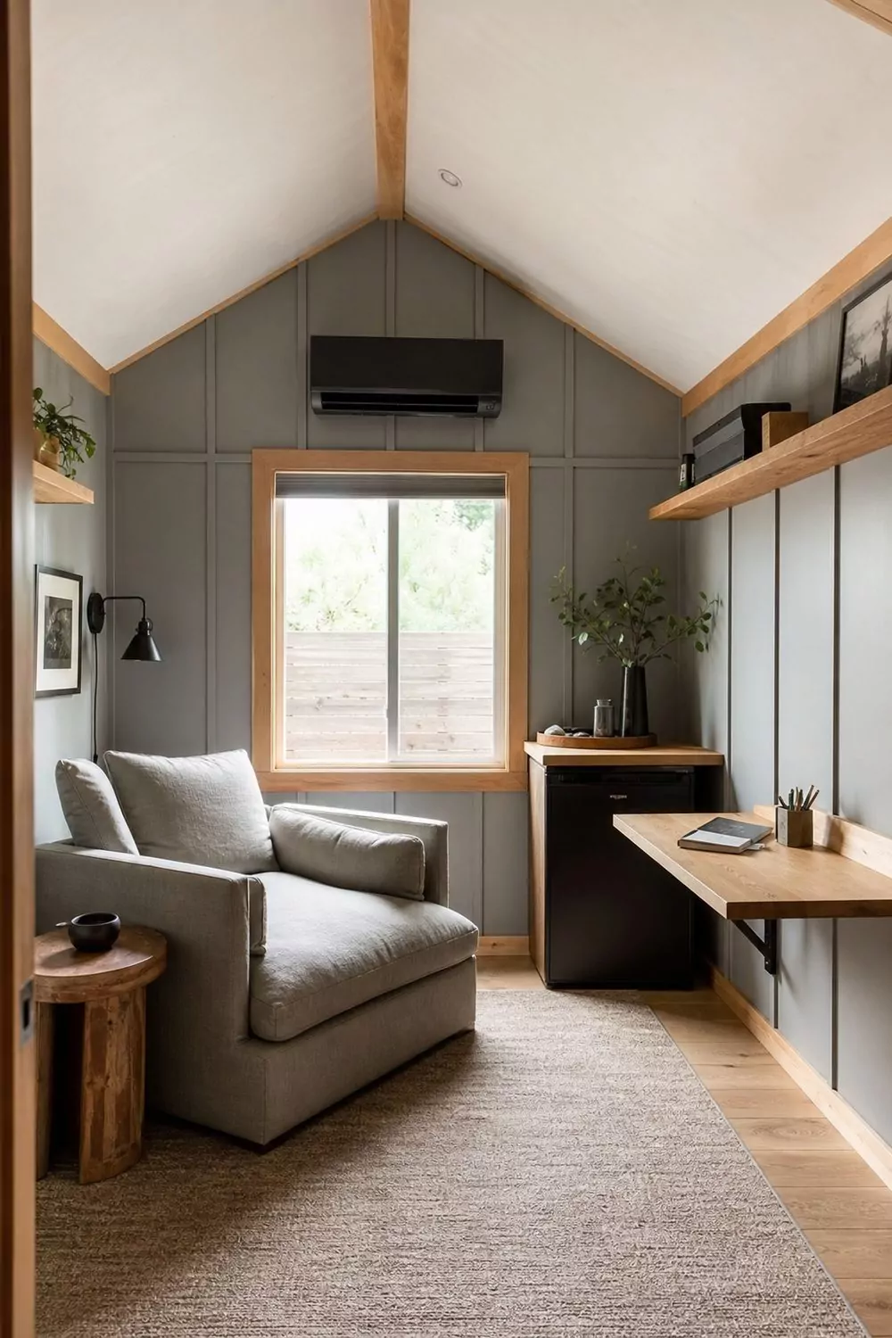 Converted backyard shed man cave retreat with painted plywood walls, oversized lounge chair, fold-down desk and a mini-split in bright daylight