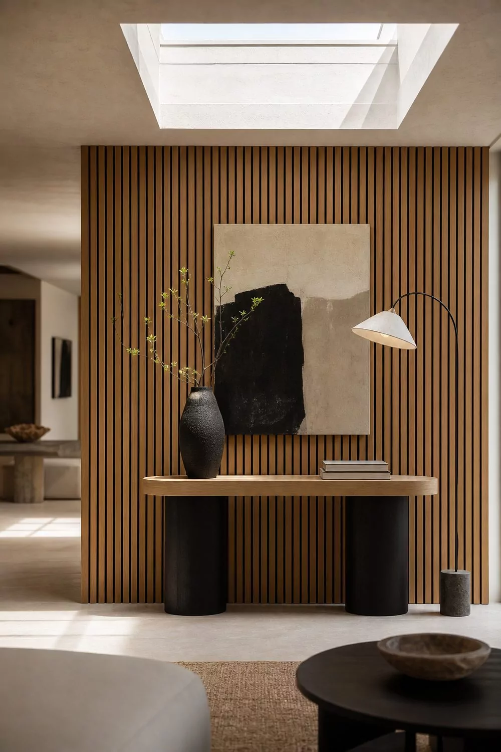 Showroom focal feature wall in slatted oak with a single styled console vignette, layered art and a tall floor lamp under directional light