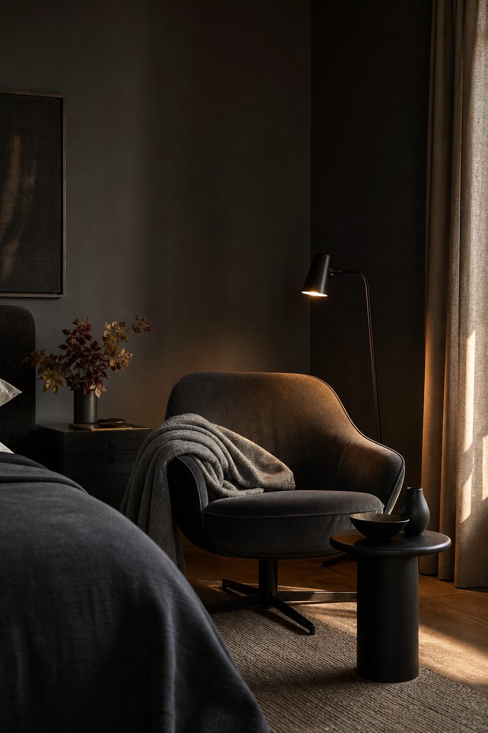 Charcoal lounge chair, small black side table and warm focused lamp in a corner reading nook of a black and grey bedroom