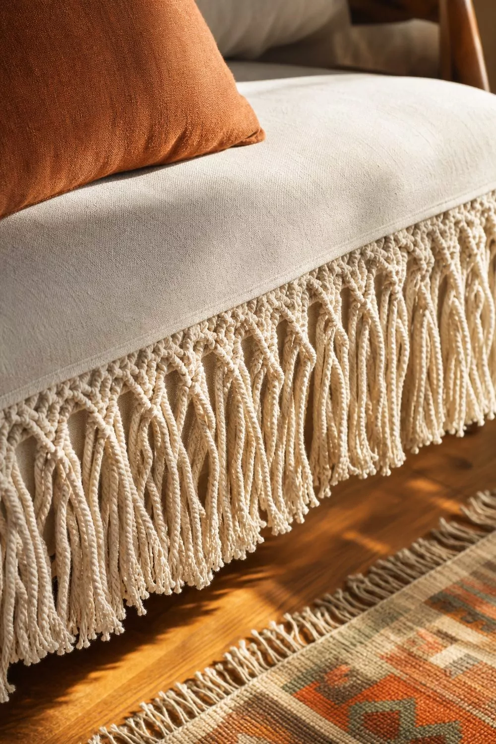 Close-up of a macrame fringe boho couch cover with hand-knotted tassels along the seat edge and terracotta pillow