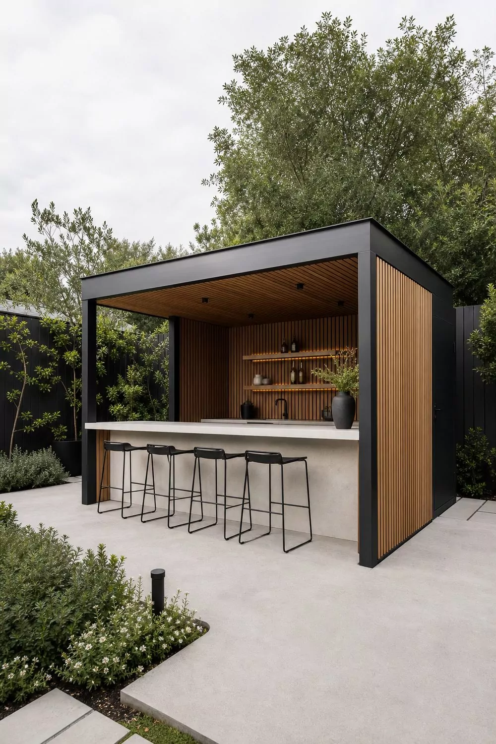 Modern backyard cabana bar with a matte black steel frame, slatted oak paneling, pale stone counter, and black stools in a contemporary yard