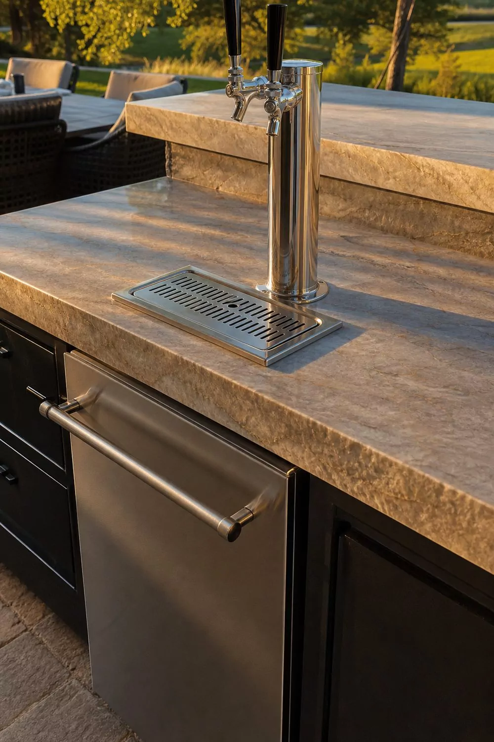 Backyard cabana bar with a polished stone slab counter, a built-in stainless kegerator, a brushed dual-tap tower, and a recessed drip tray at golden hour