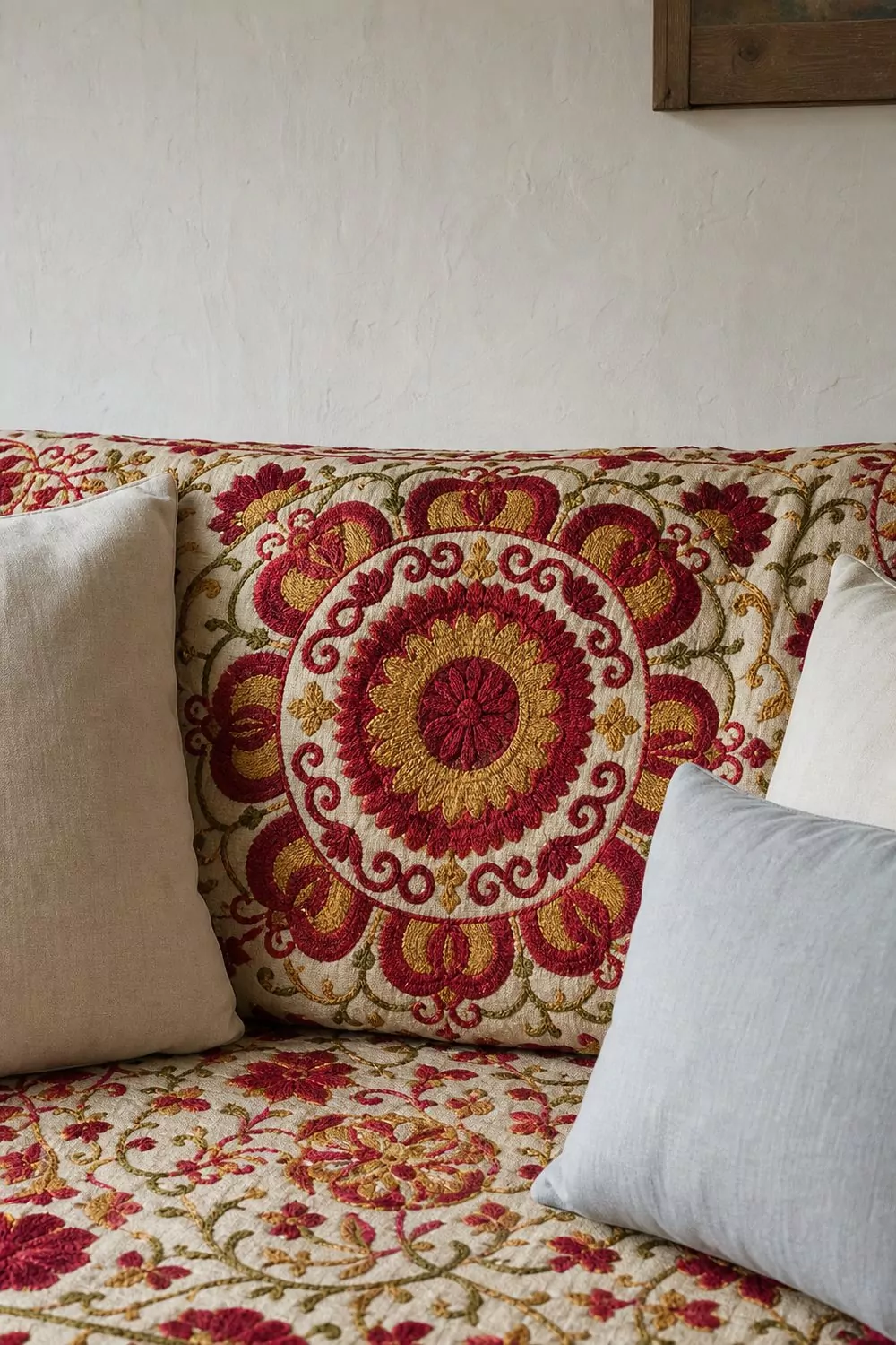 Suzani embroidered boho couch cover with crimson and gold medallion motifs in raised stitching on neutral sofa