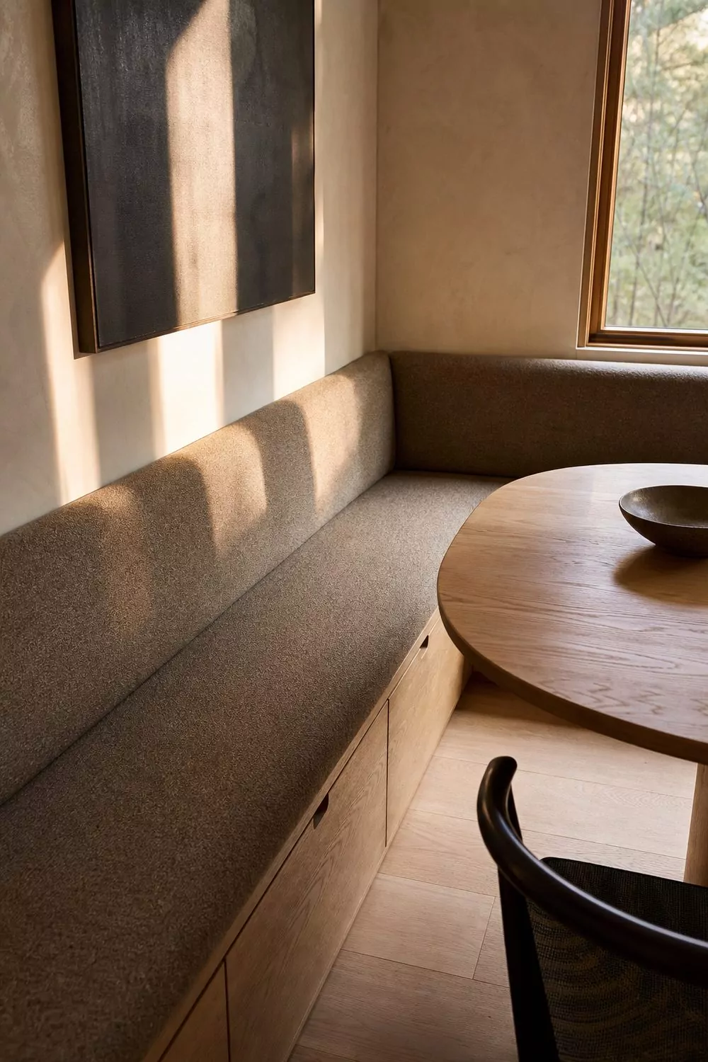L shaped built in banquette with taupe cushion and oak storage drawers below beside an oval table in a contemporary dining nook