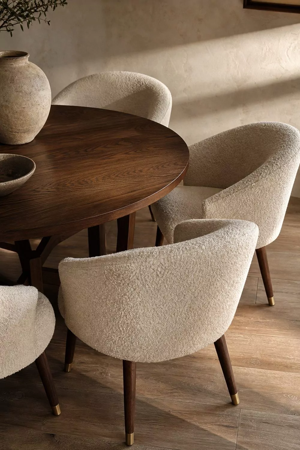 Four cream boucle barrel back dining chairs arranged around a round dark walnut table in a contemporary dining room