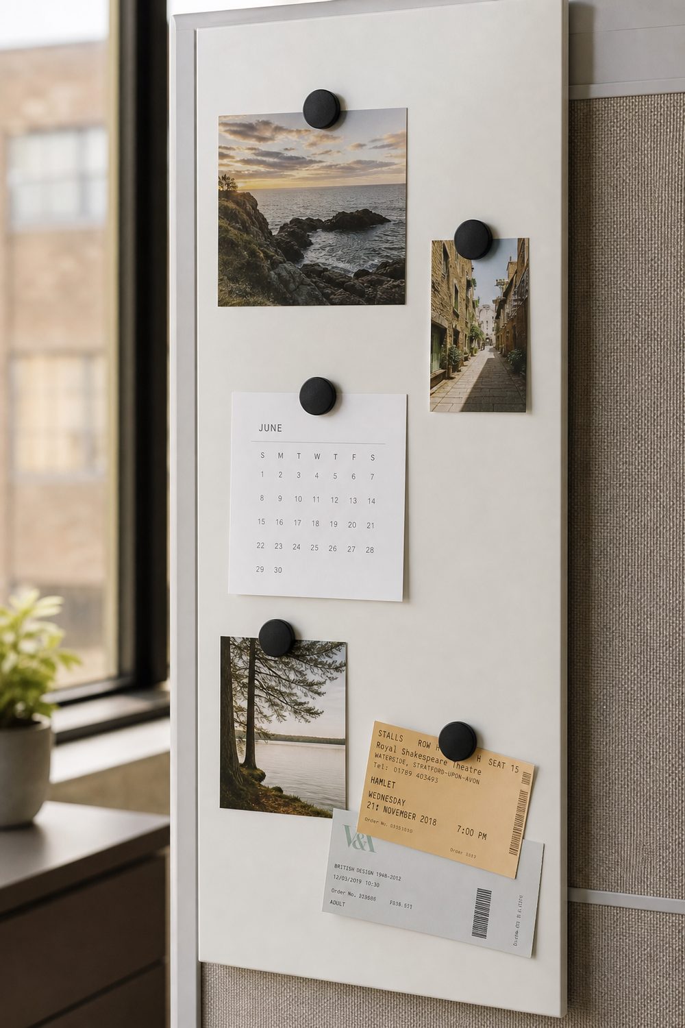 Slim white magnetic board on a cubicle panel holding family photos, a monthly calendar, and event tickets with round magnets