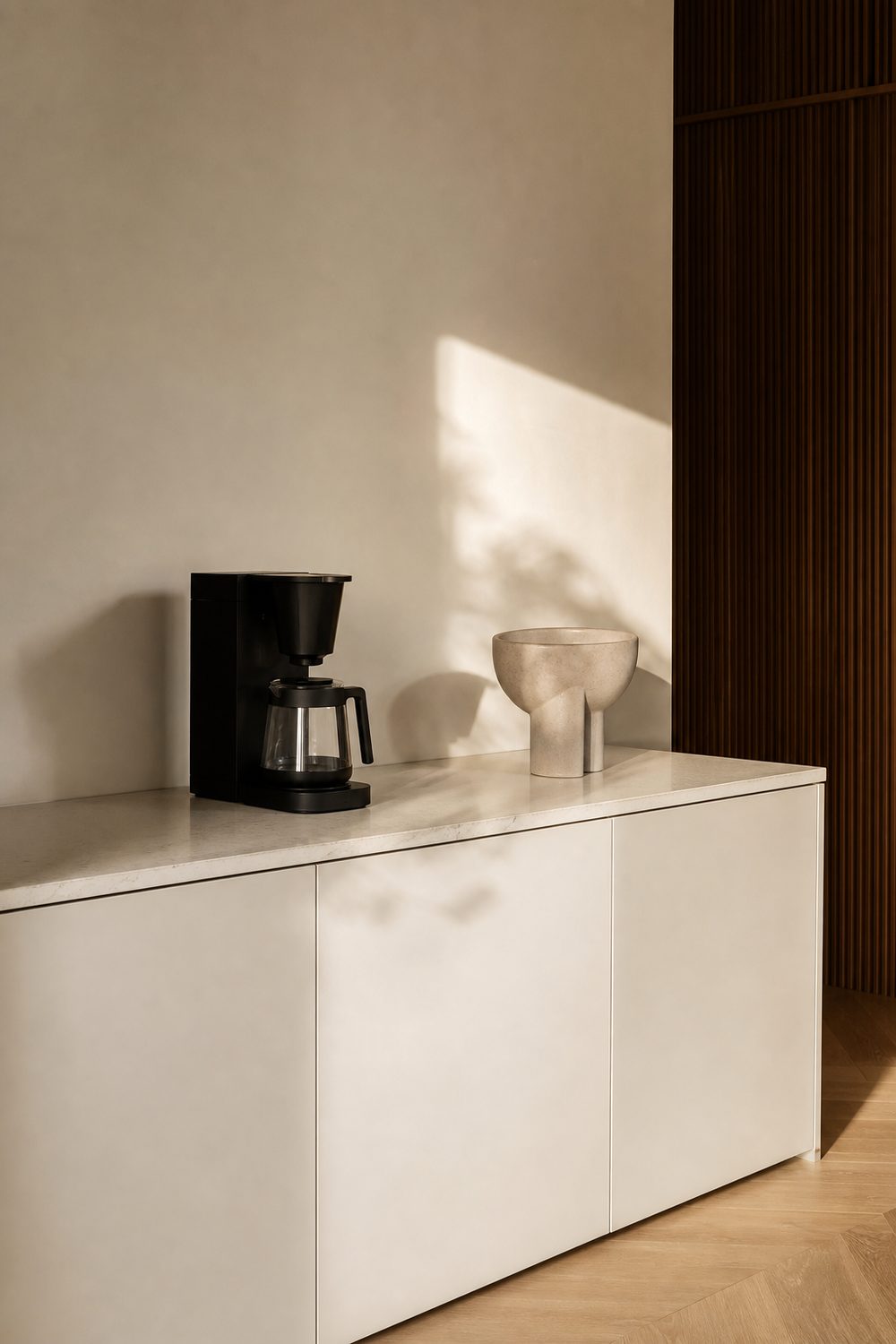 Modern minimalist coffee station with matte white cabinetry, a slim black machine, and a single sculptural vessel