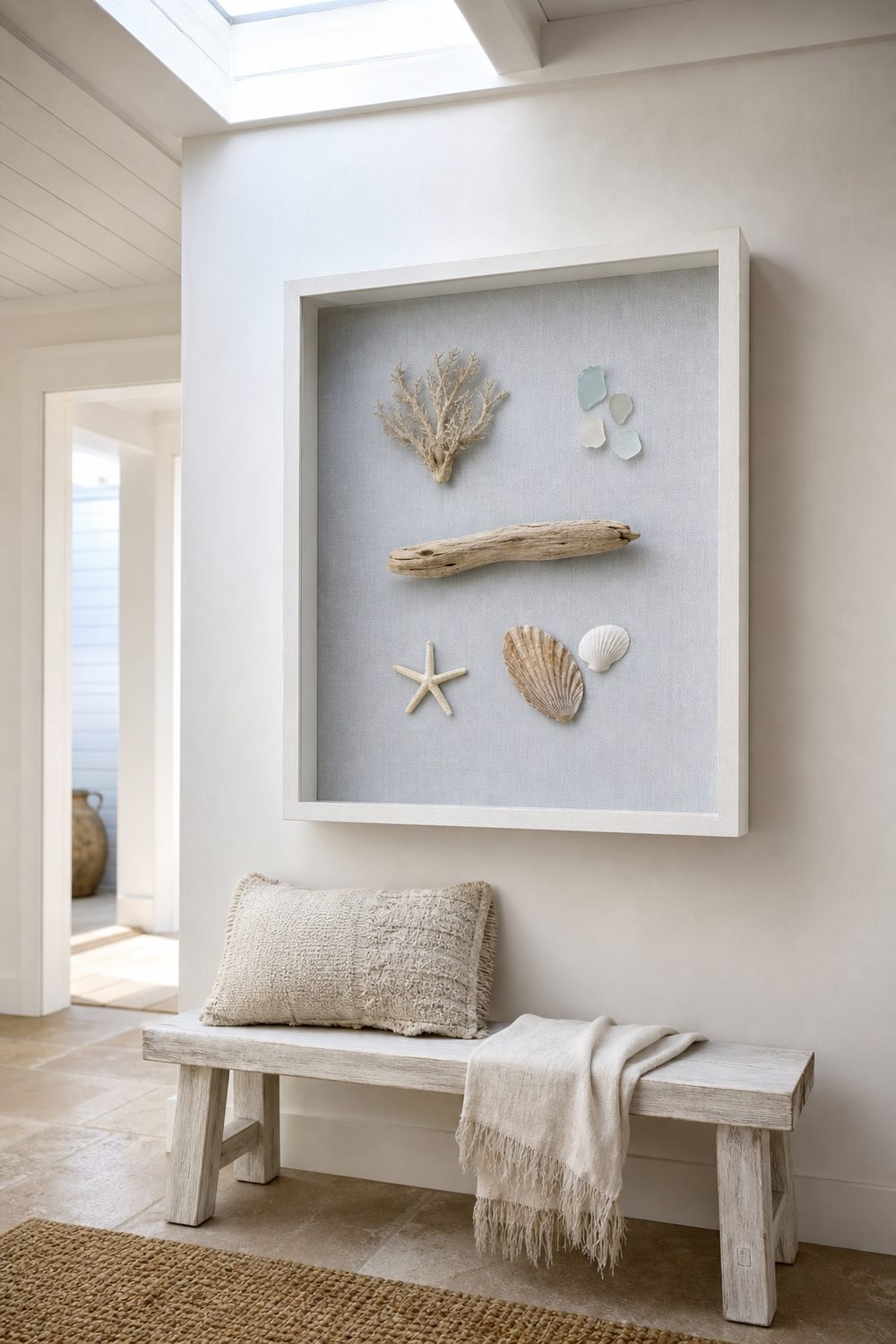 Seashell shadow box with grouped shells, driftwood and sea glass on pale blue-gray linen in a deep white frame