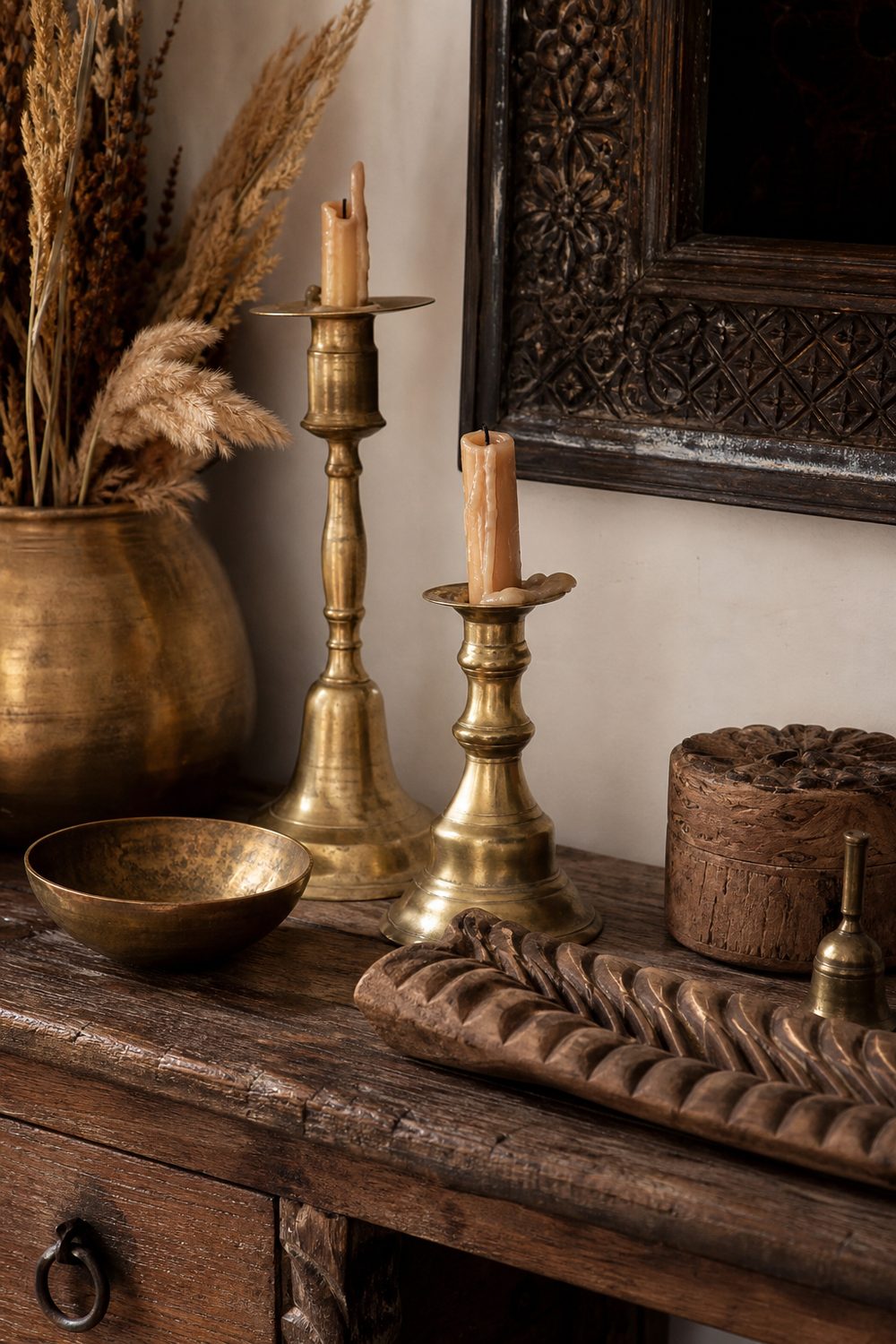 Close-up of vintage brass candlesticks and carved wooden objects on a reclaimed wood console in a boho room