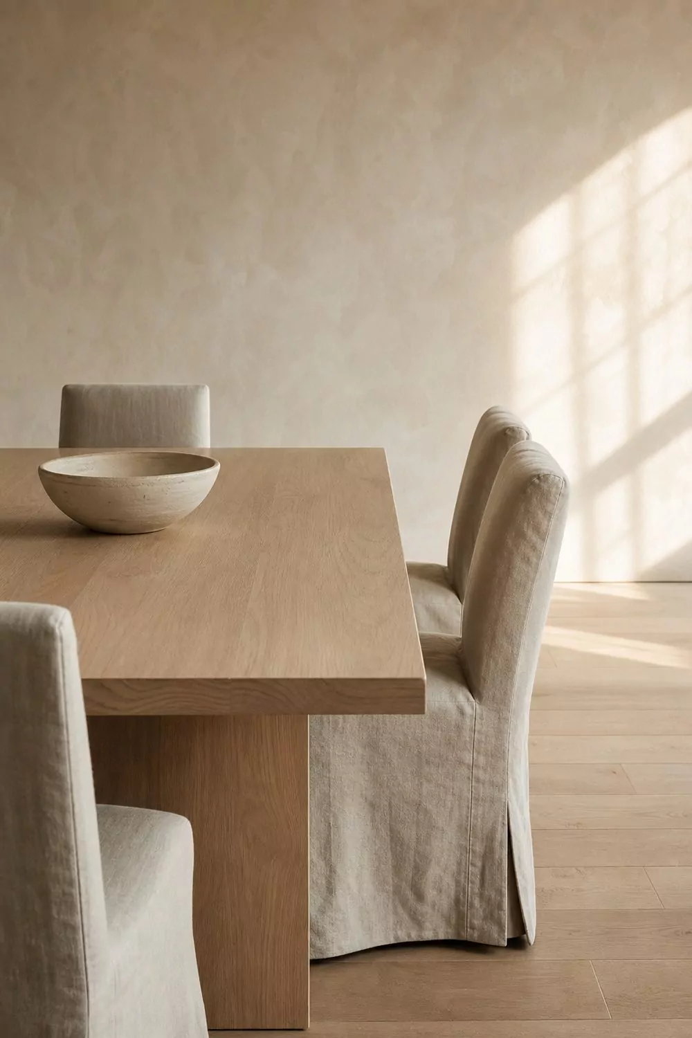 Warm minimalist contemporary dining room with pale oak table, greige linen slipcovered chairs and off white limewash walls