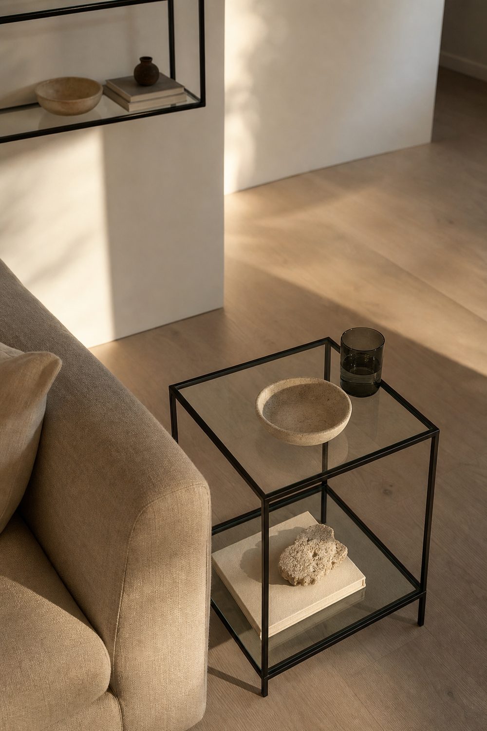 Slim black steel and glass side table beside a linen sofa in a warm neutral minimalist living room