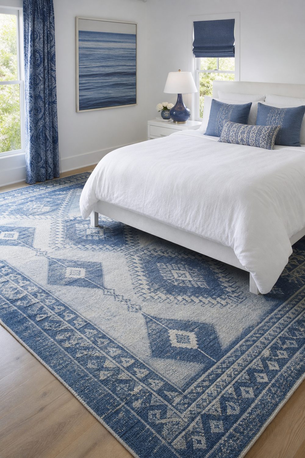 Large blue and white patterned wool area rug on pale oak floor beneath a simple white bed with plain white bedding
