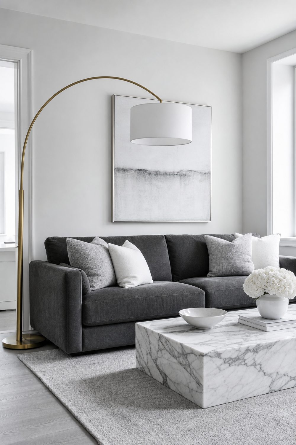 Brass arc floor lamp curving over a charcoal grey sofa with white marble coffee table and pale grey rug