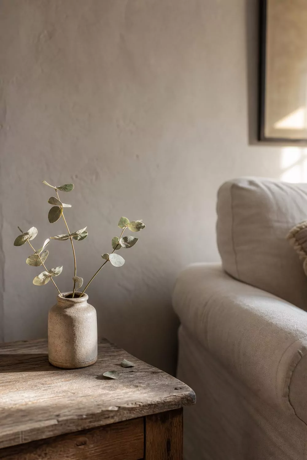 Small bunch of dried silver green eucalyptus in a matte stoneware crock on a worn oak farmhouse side table