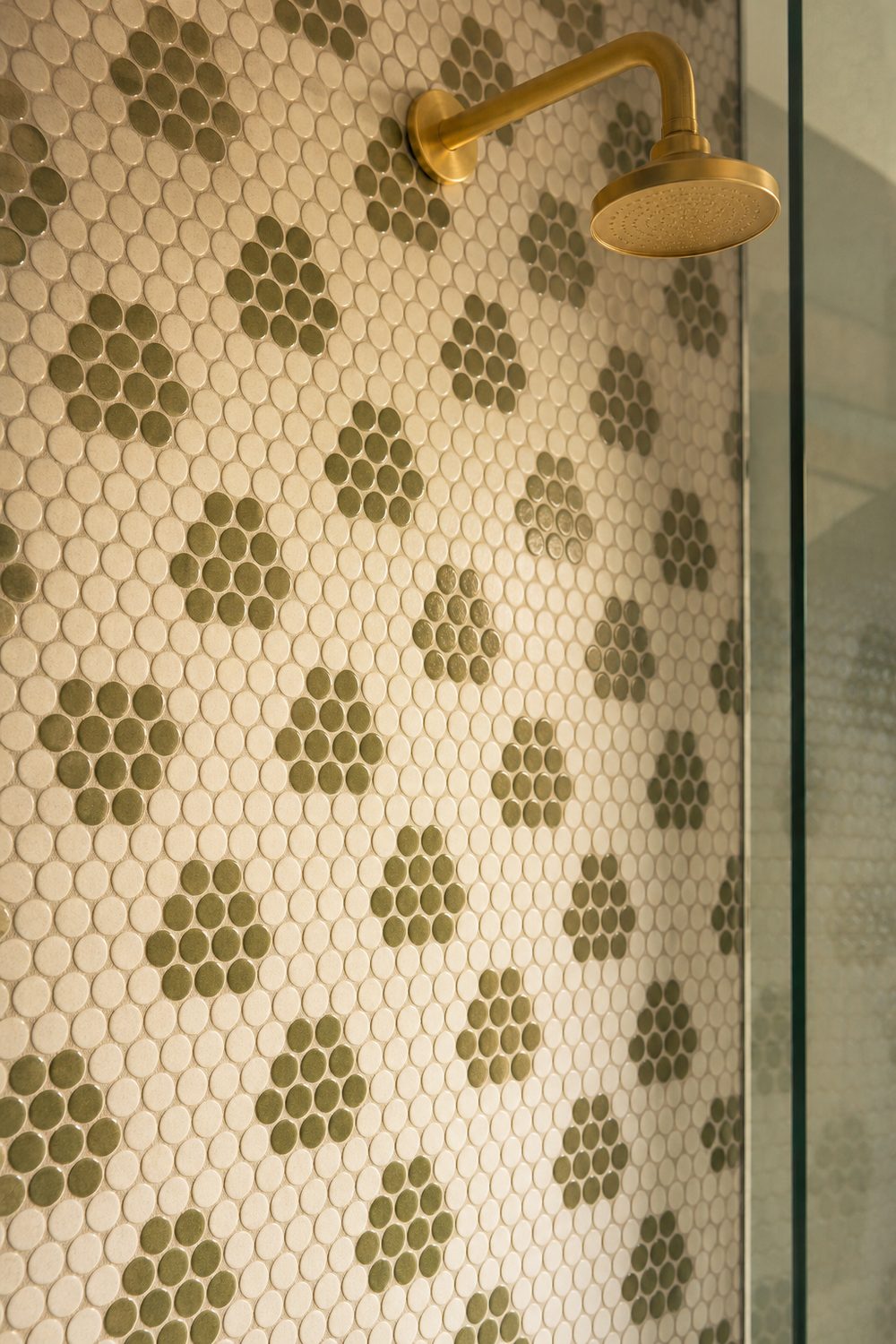 Olive and cream penny tile shower wall in repeating flower clusters with a brushed brass shower arm and head