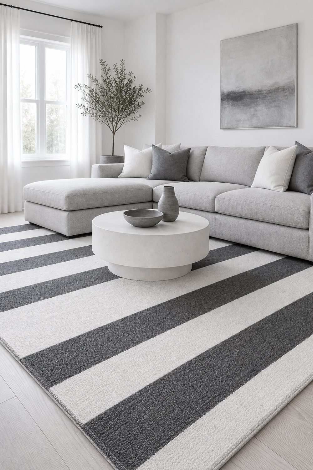 Charcoal and white striped area rug under a grey sectional and round white coffee table in a white walled living room
