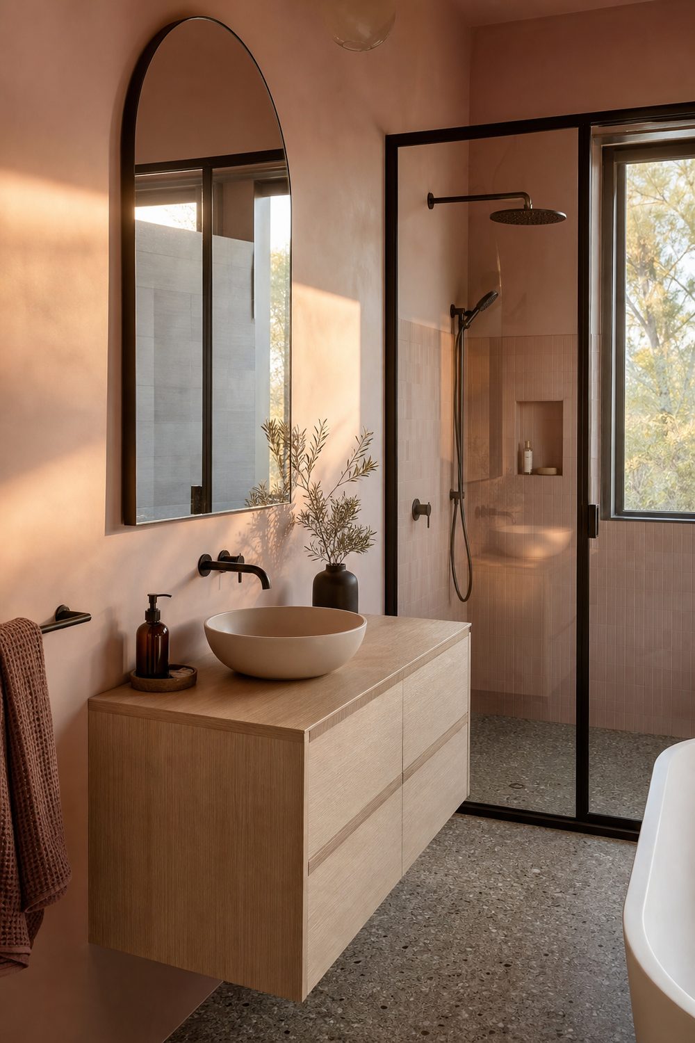 Pale pink painted walls with matte black tapware, towel bars and shower screen frame, alongside a white oak floating vanity