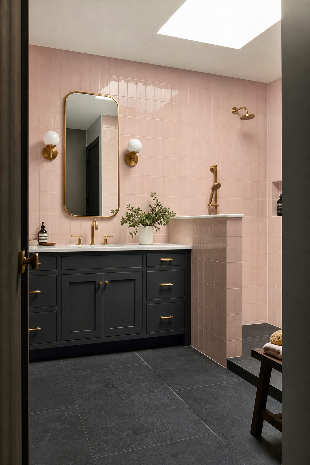 Pink wall tile meeting a charcoal grey tiled floor, with a charcoal painted vanity and warm brass hardware between them