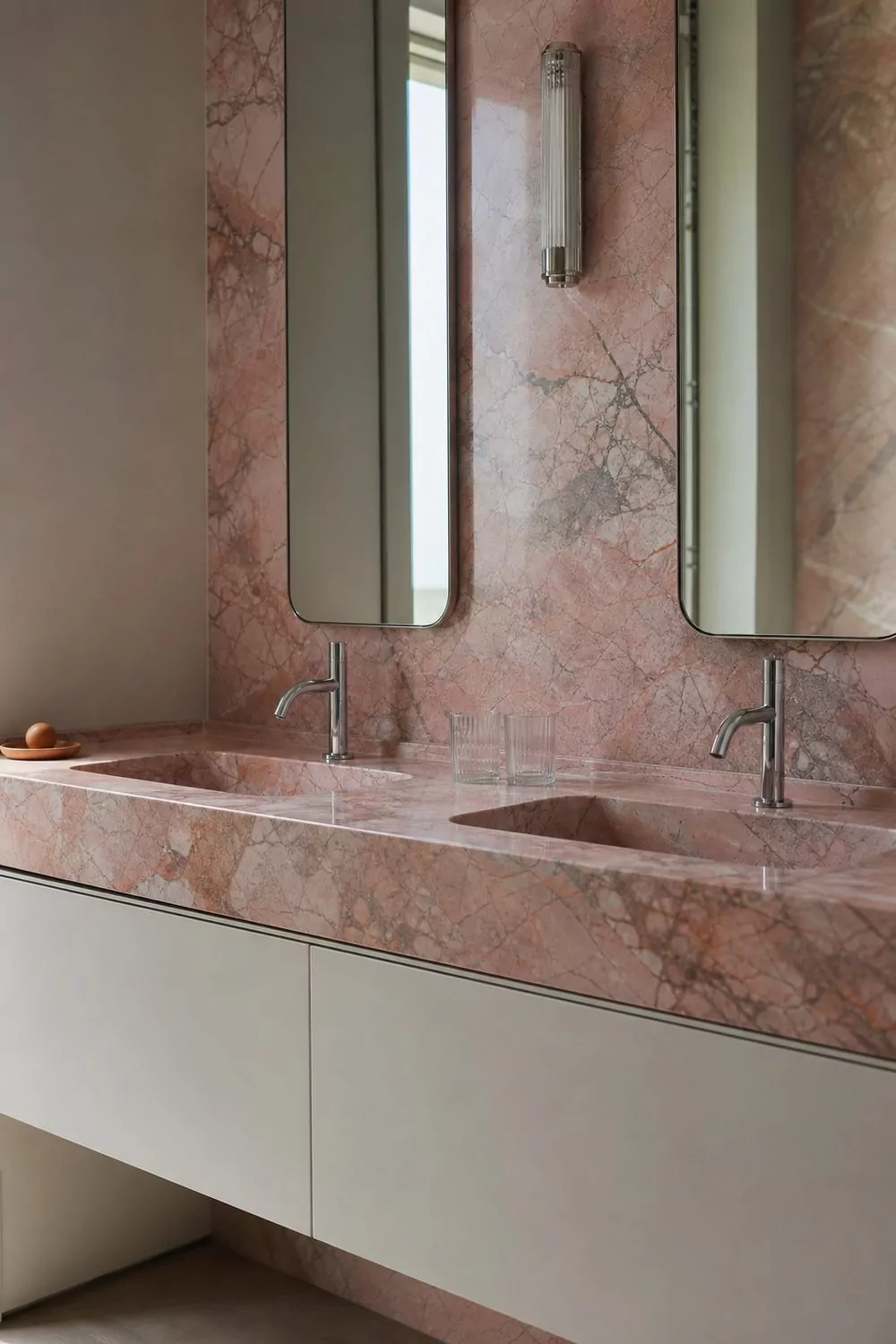 Double vanity with a honed pink marble countertop run up the wall as a full height slab backsplash, twin basins and chrome faucets