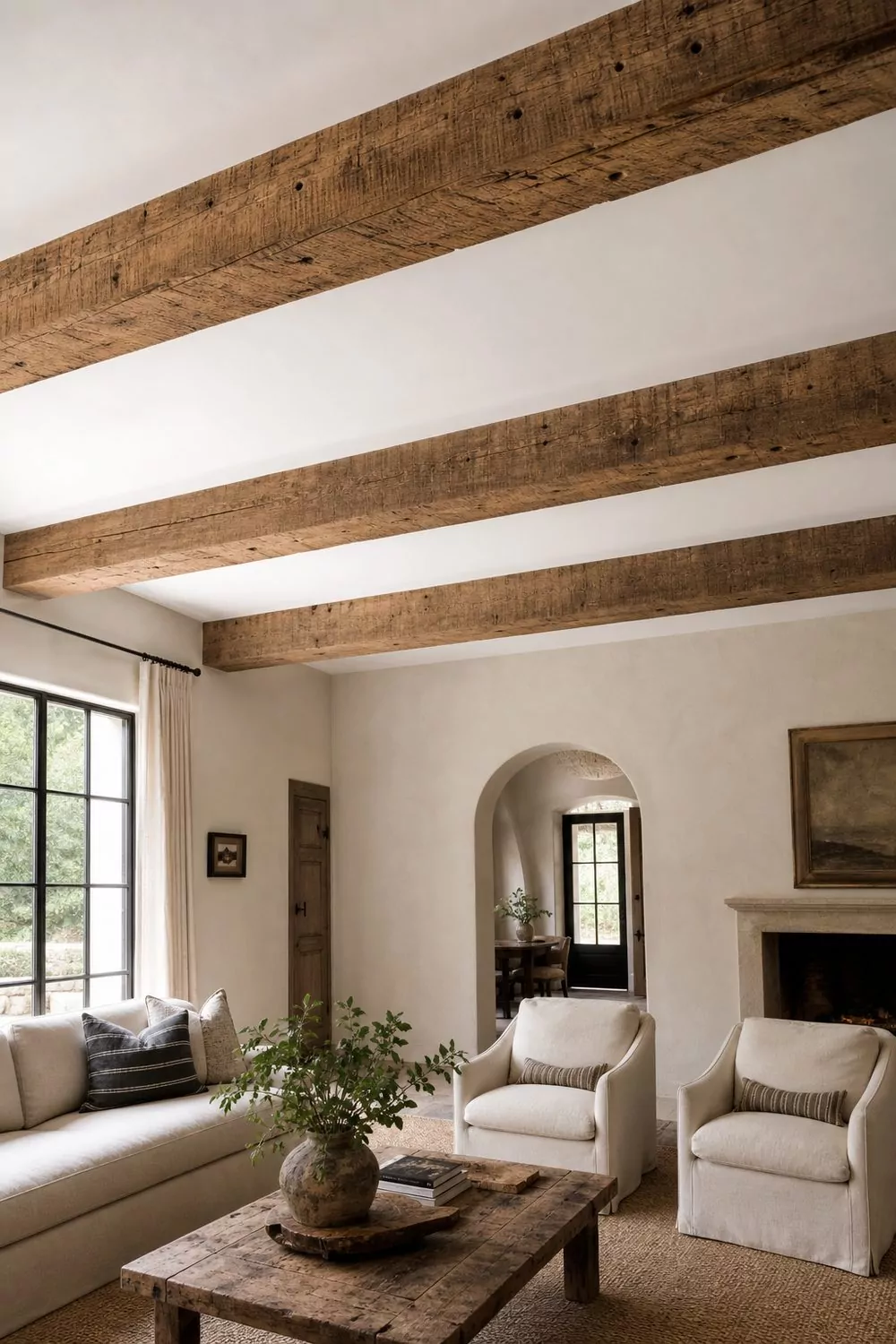 Three reclaimed oak box beams across a white farmhouse living room ceiling above a neutral seating group