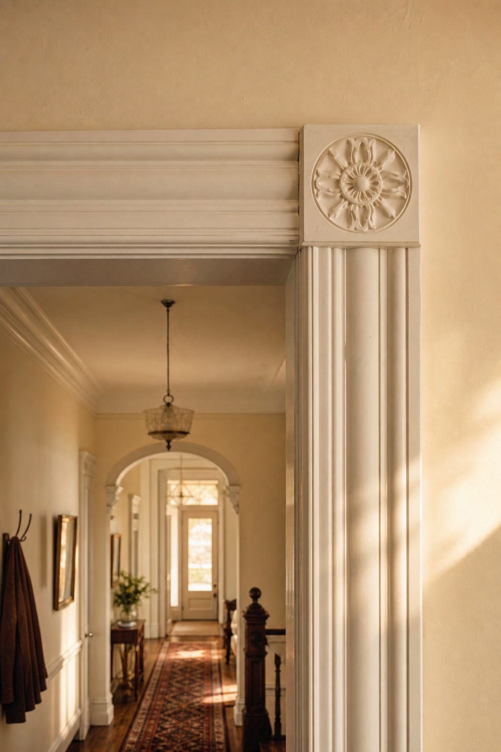 Carved white rosette corner blocks joining fluted door casing legs at the top corners in a cream Victorian hallway