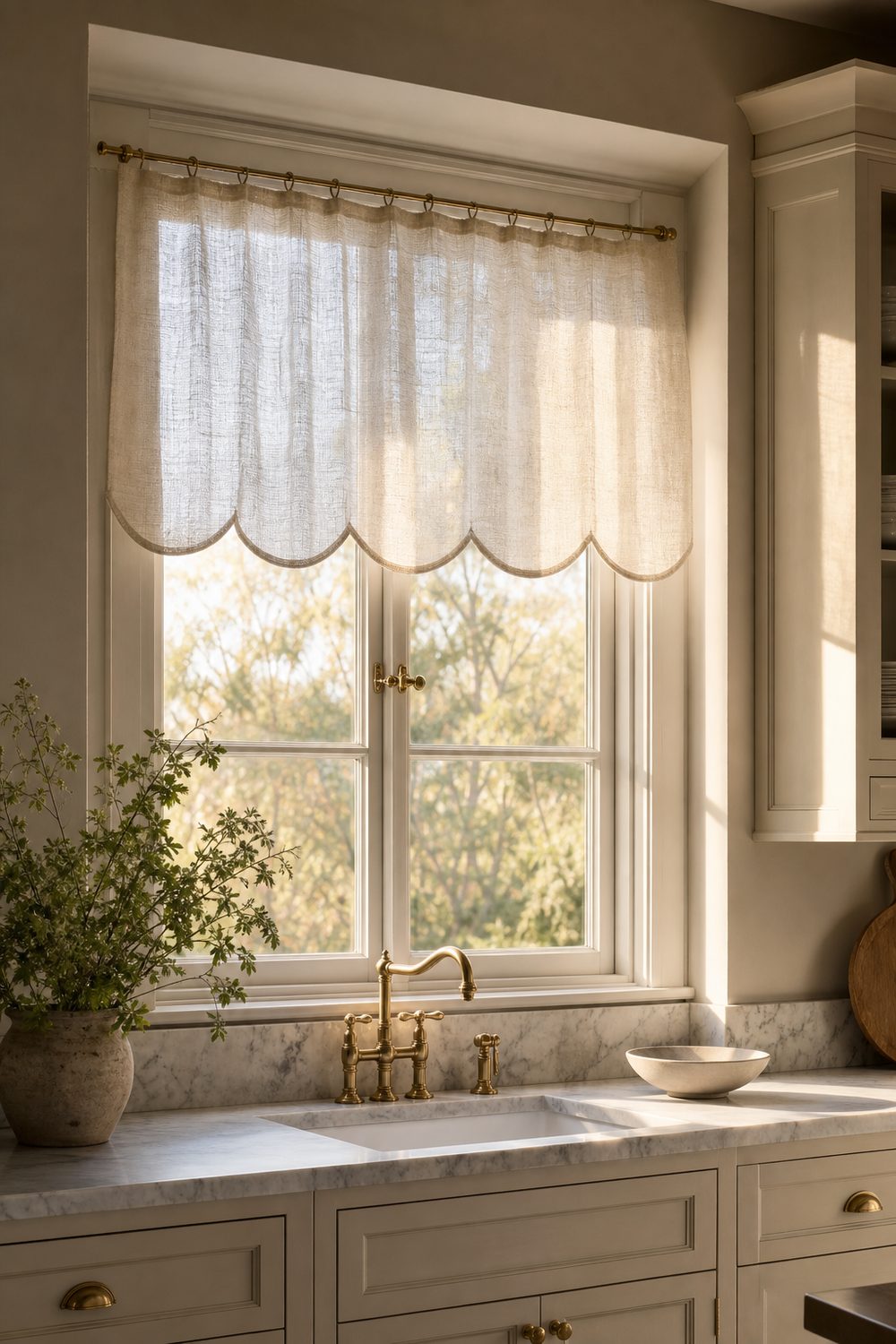 Sheer oatmeal linen valance with a scalloped hem above a neutral kitchen window with marble counters