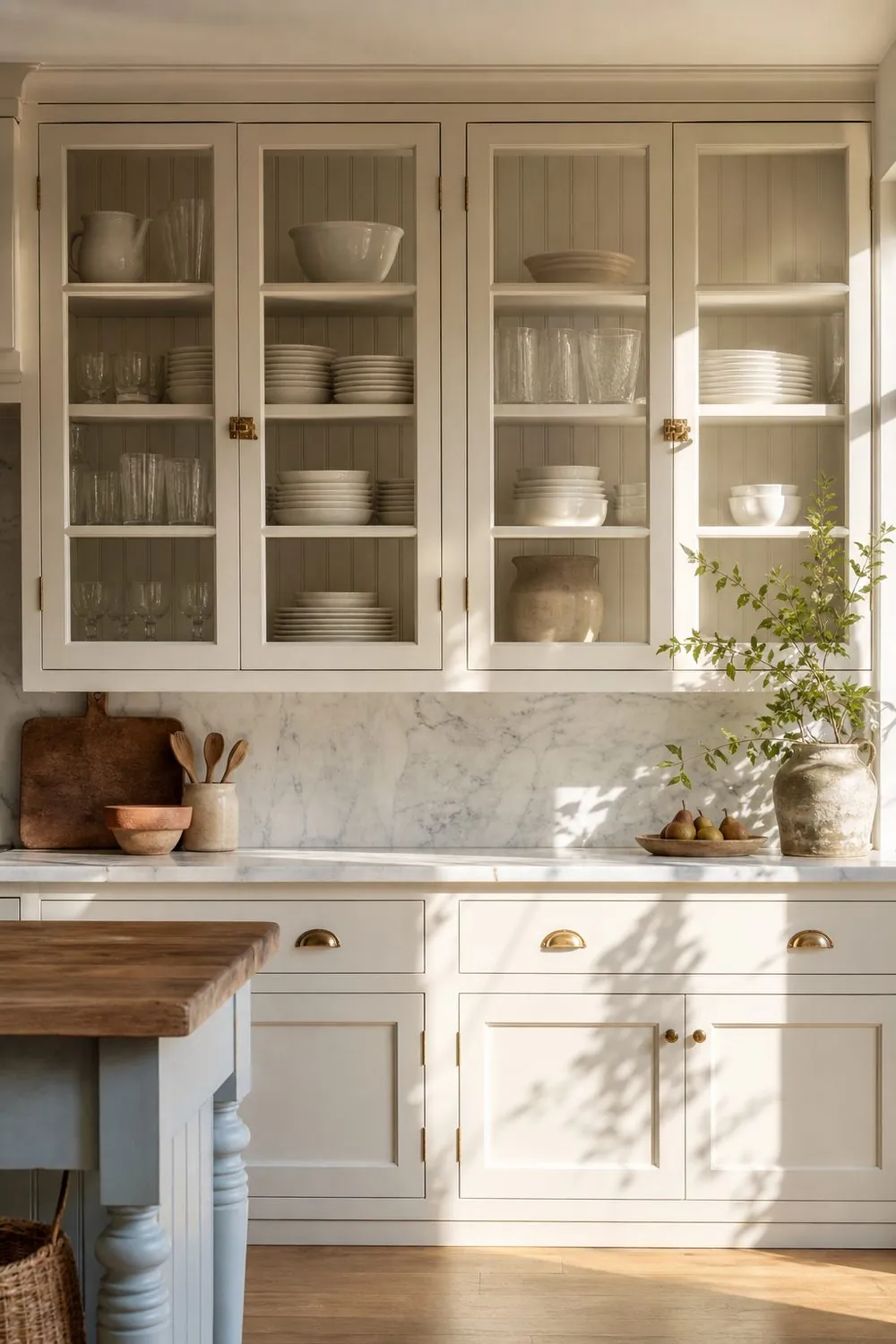 Glass front upper cabinets with white beadboard backing and brass latches showing stacked dishes above a marble counter in a farmhouse kitchen