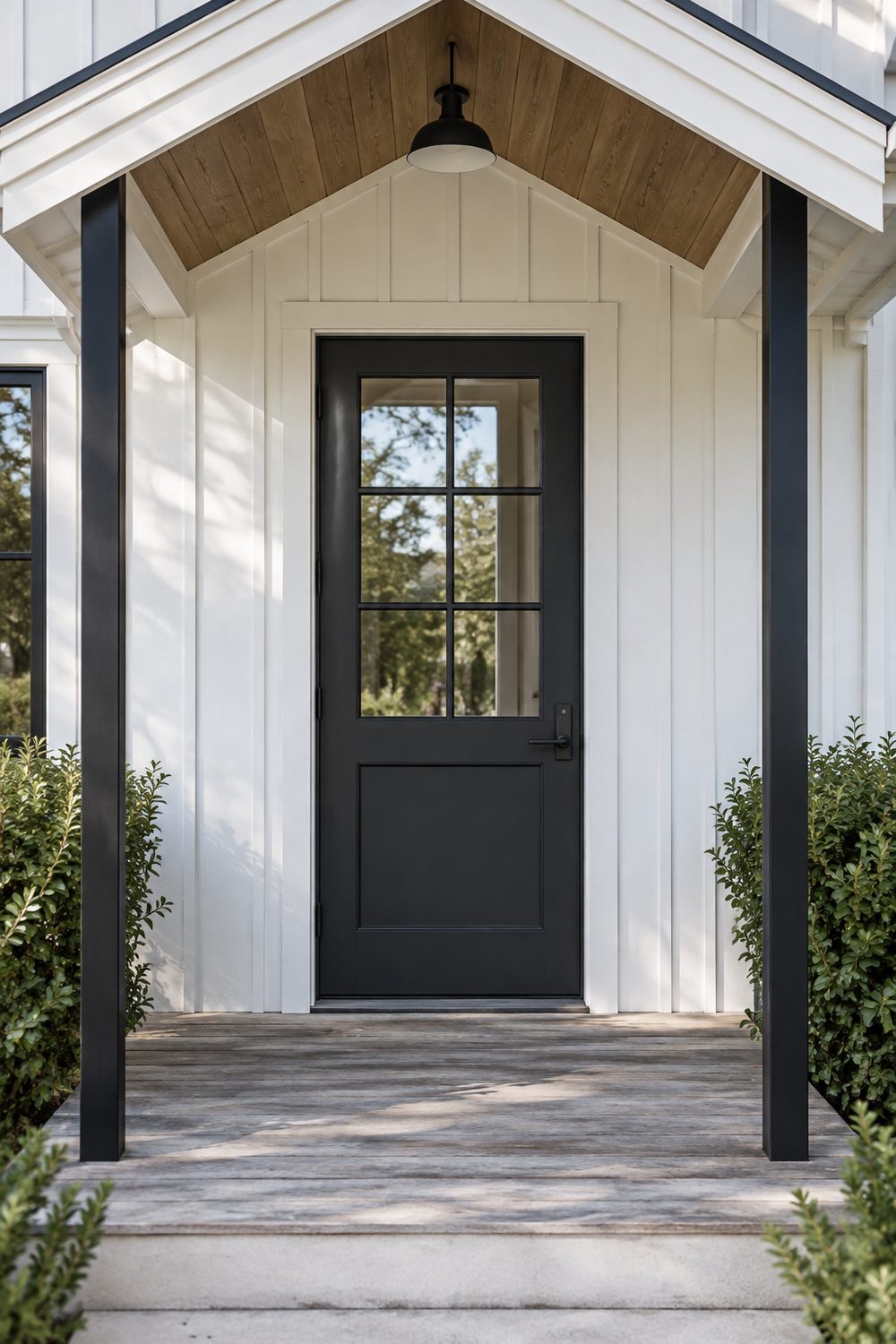 Charcoal modern farmhouse front door with six glass panes in the upper half under a small gabled porch with black posts