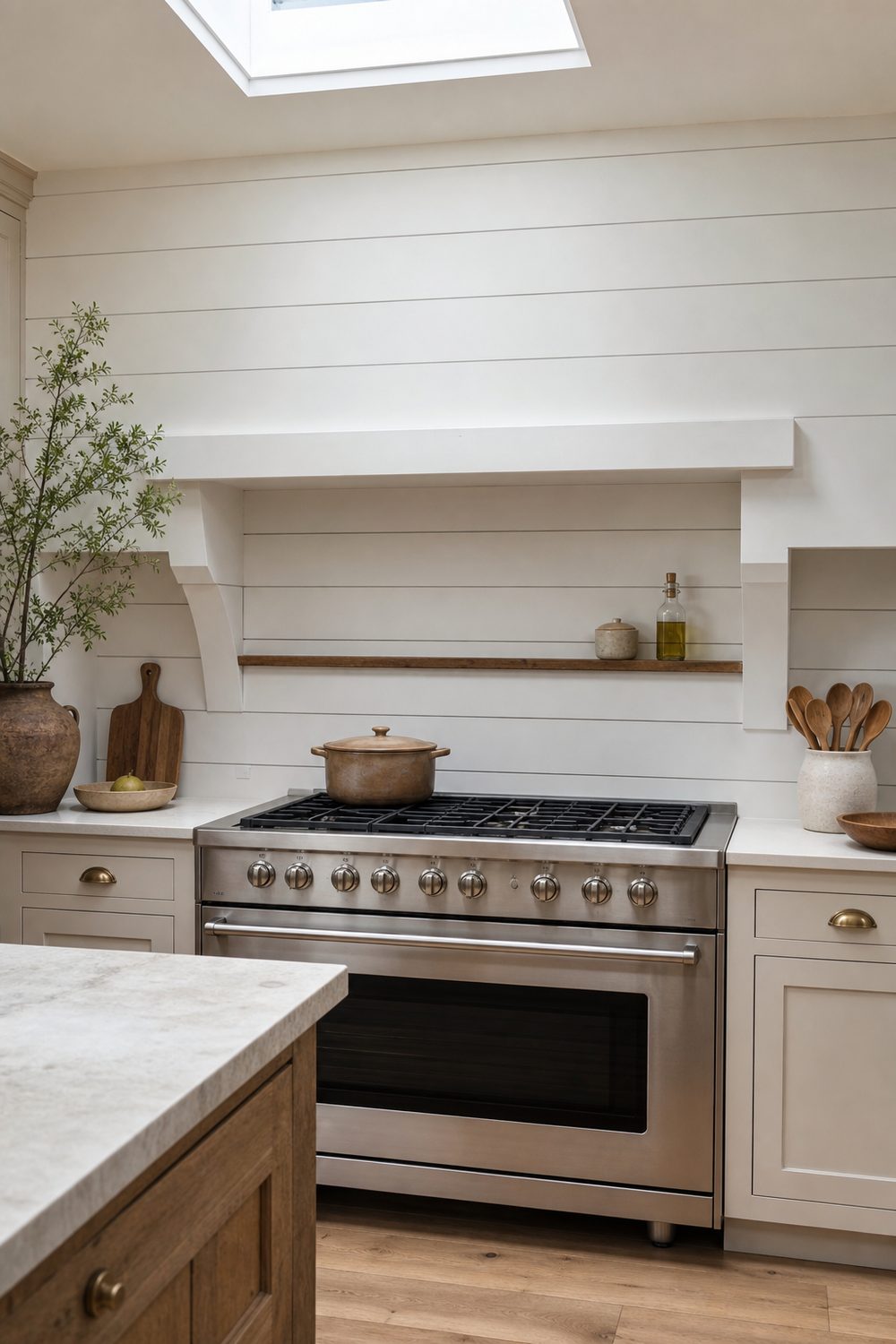 Painted white shiplap backsplash with horizontal board seams behind a range in a farmhouse kitchen, flanked by cabinets and a small wood ledge