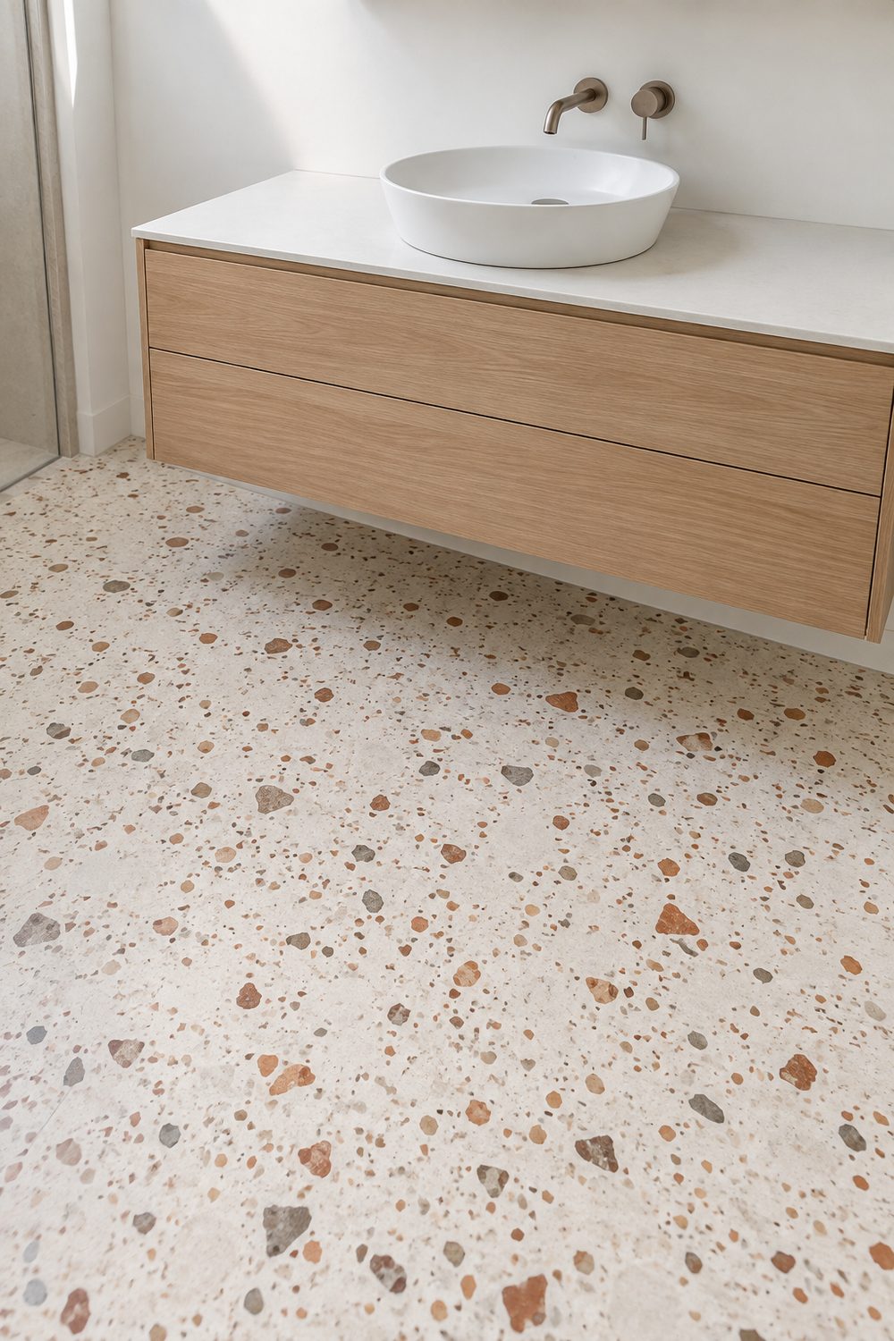 Pale cream terrazzo bathroom floor with terracotta and grey chips, light oak floating vanity and a plain white wall