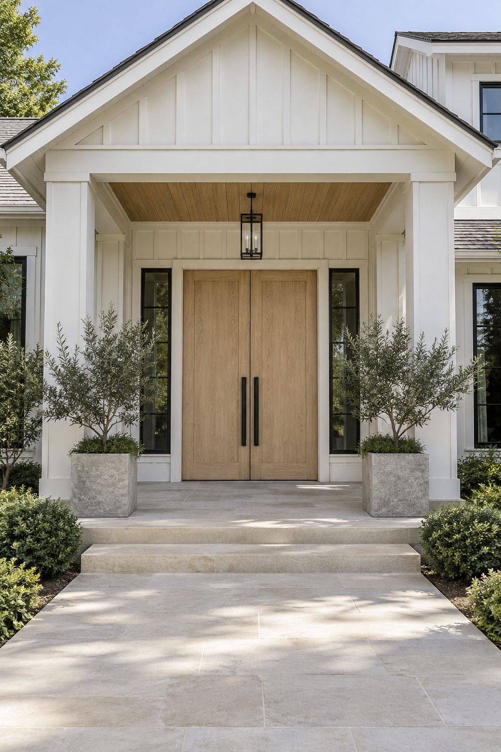 Pair of tall white oak double front doors with long black pulls under a covered entry with white board and batten siding